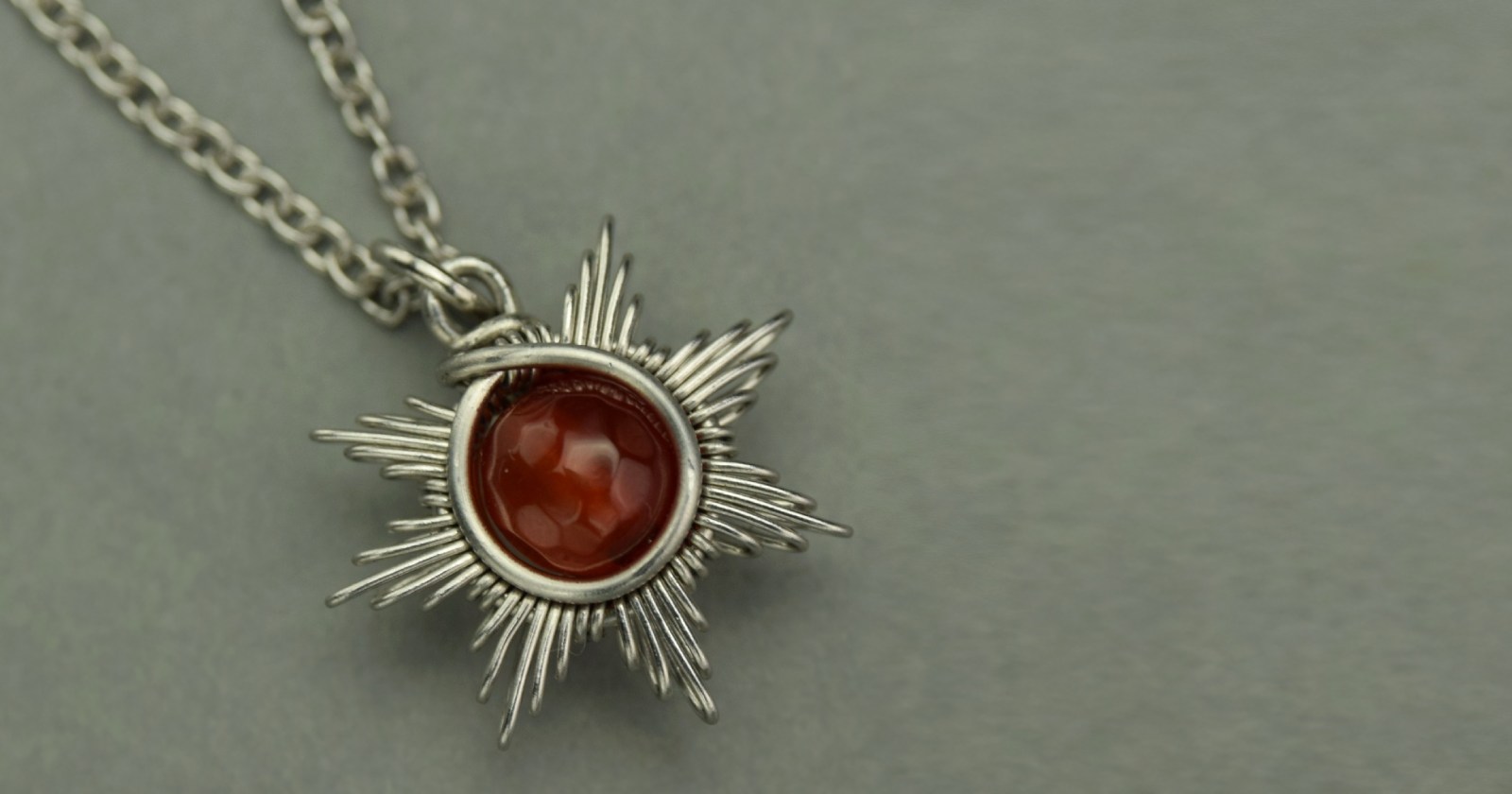 Mały wisiorek w kształcie słońca z kulką karneolu. Wykonany ręcznie techniką wire wrapping z drutów ze stali chirurgicznej